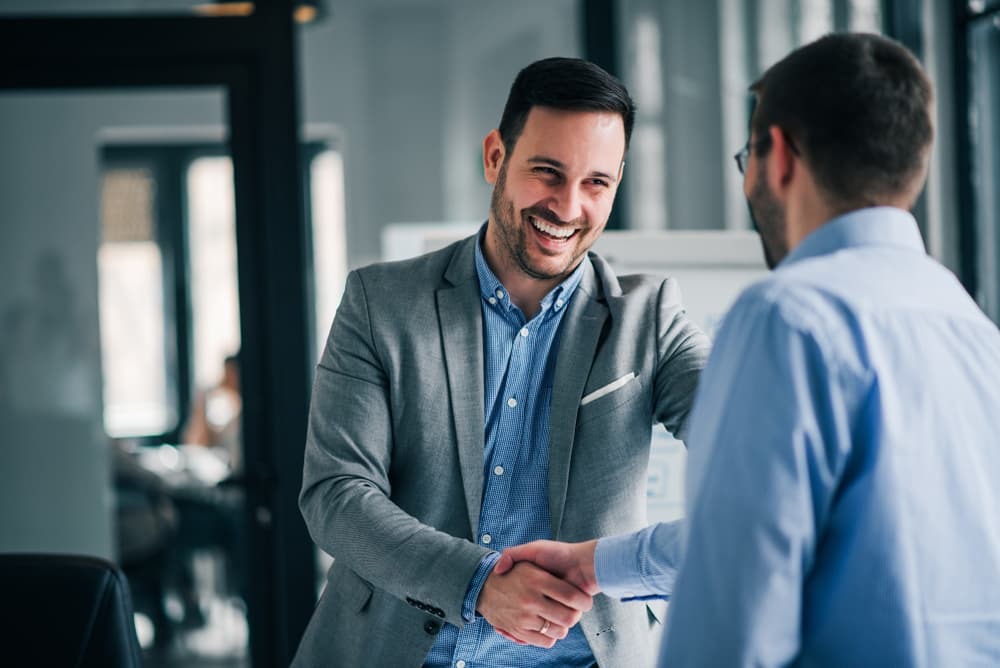Two professionals shaking hands in a formal office setting, symbolizing a successful business deal.